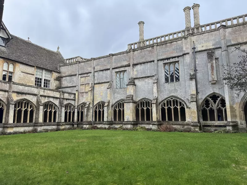 A large gray stone building with gothic arches on the ground level and a green grass yard.