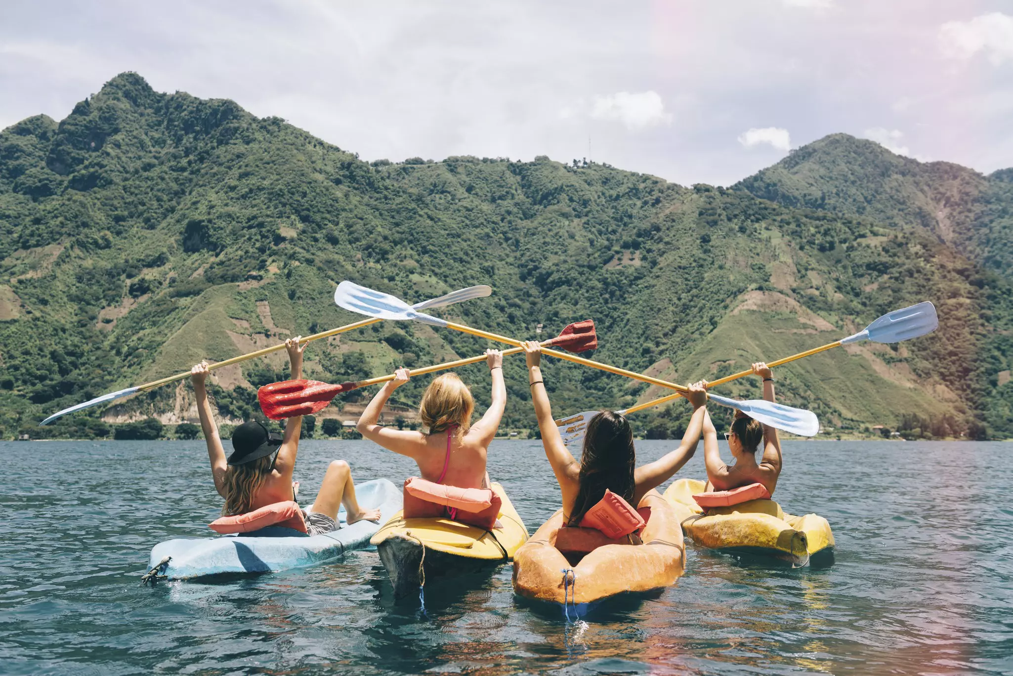 Rear view of four female friends celebrating in kayaks on Lake Atitlán, Guatemala