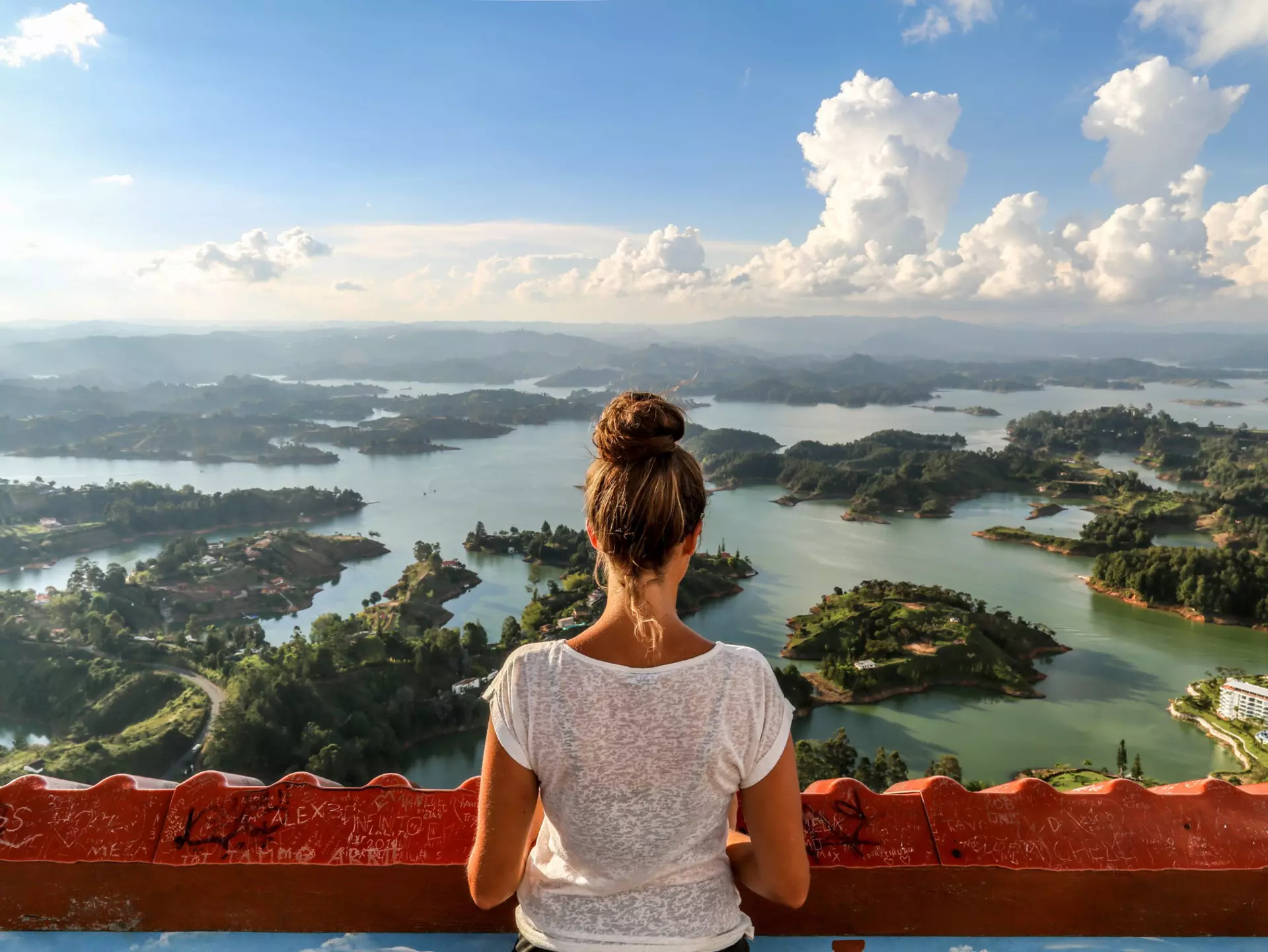 A girl seen from behind, looking out over Guatape and the expansive lake system.
