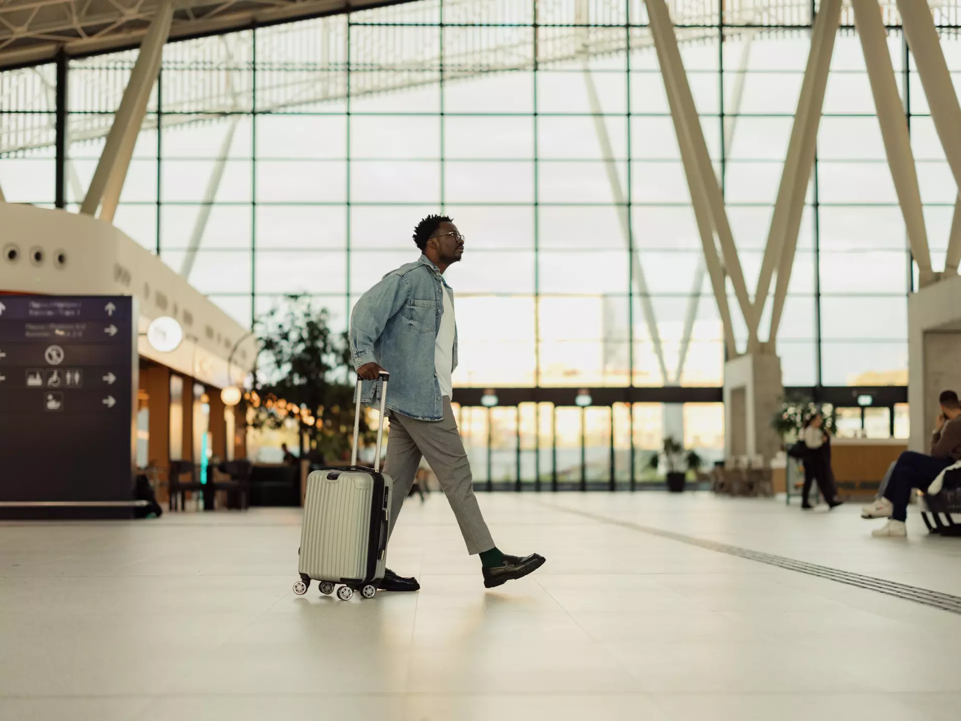 A man walks through a modern airport wheeling along his one piece of luggage for his vacation.