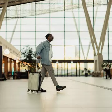 A man walks through a modern airport wheeling along his one piece of luggage for his vacation.