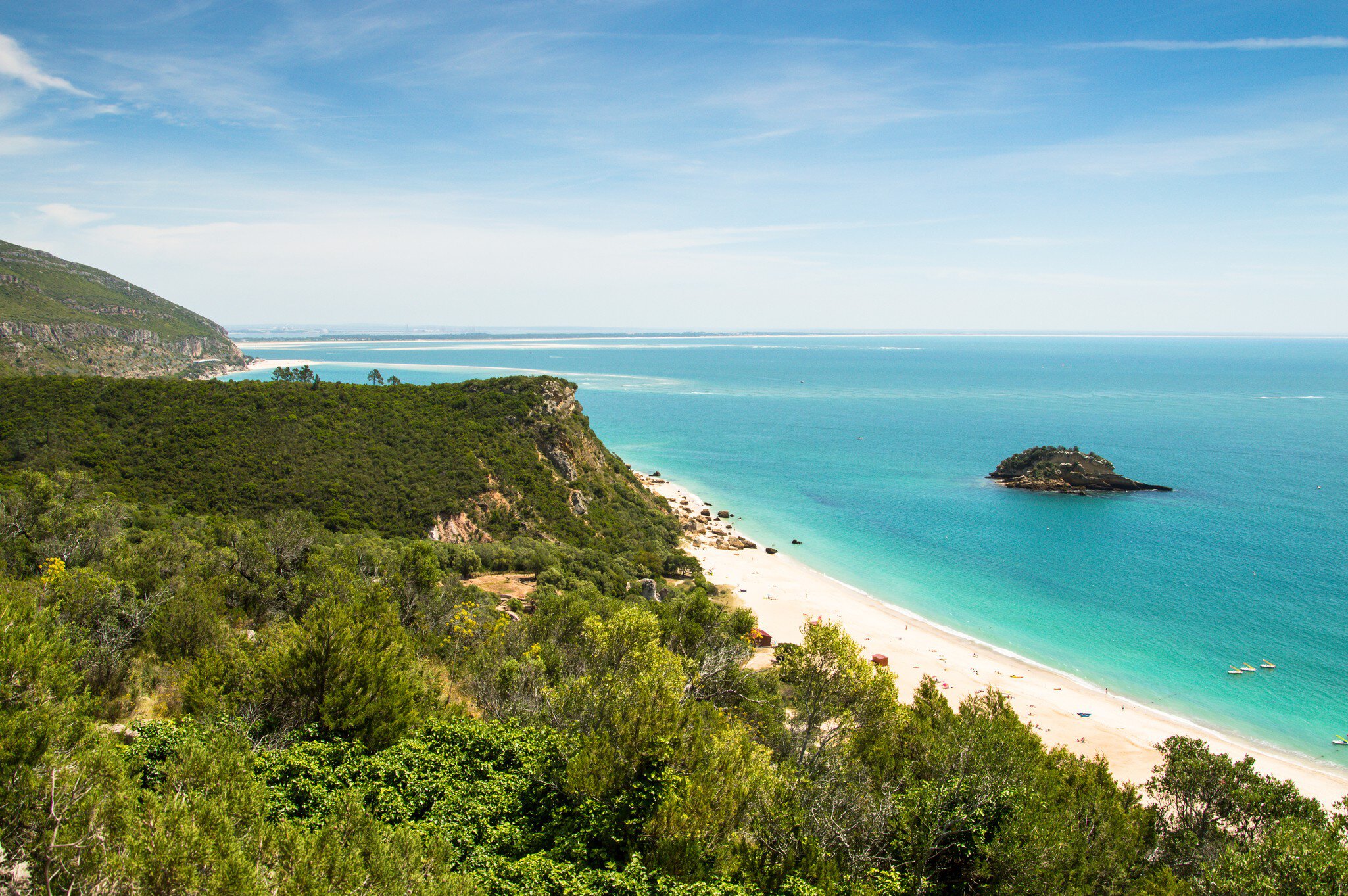 Foliage-covered cliffs dip down to a white sand beach lapped by turquoise waters.