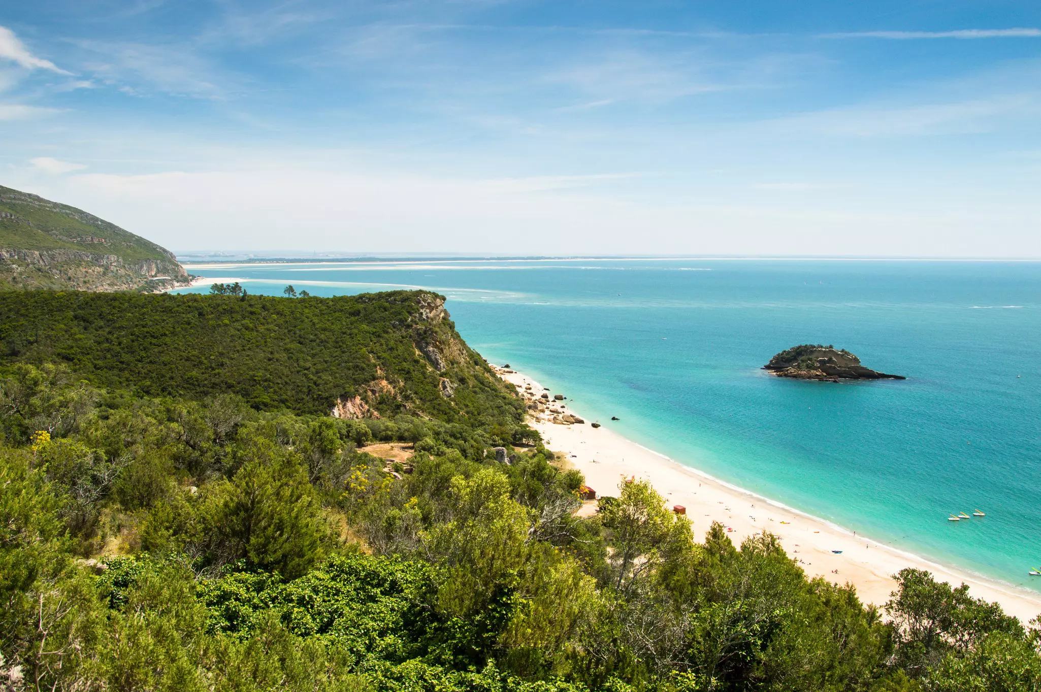 Foliage-covered cliffs dip down to a white-sand beach lapped by turquoise waters