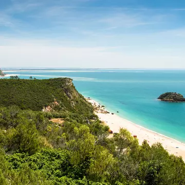 Foliage-covered cliffs dip down to a white sand beach lapped by turquoise waters.