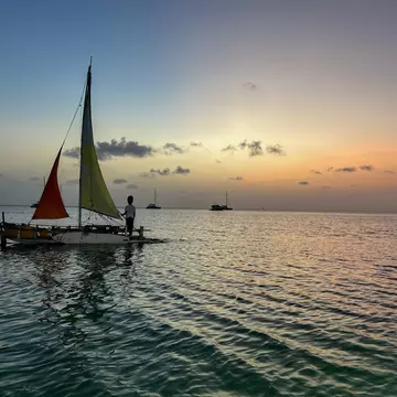A small sailboat on the sea is silhouetted in the light of sunset.