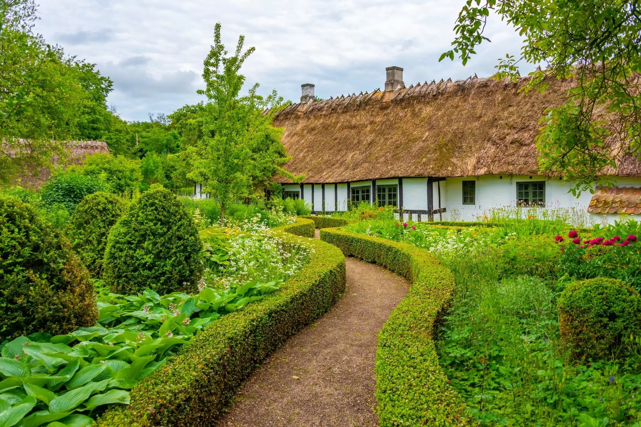 A path through a tidy green garden leads to historic thatched-roof houses.