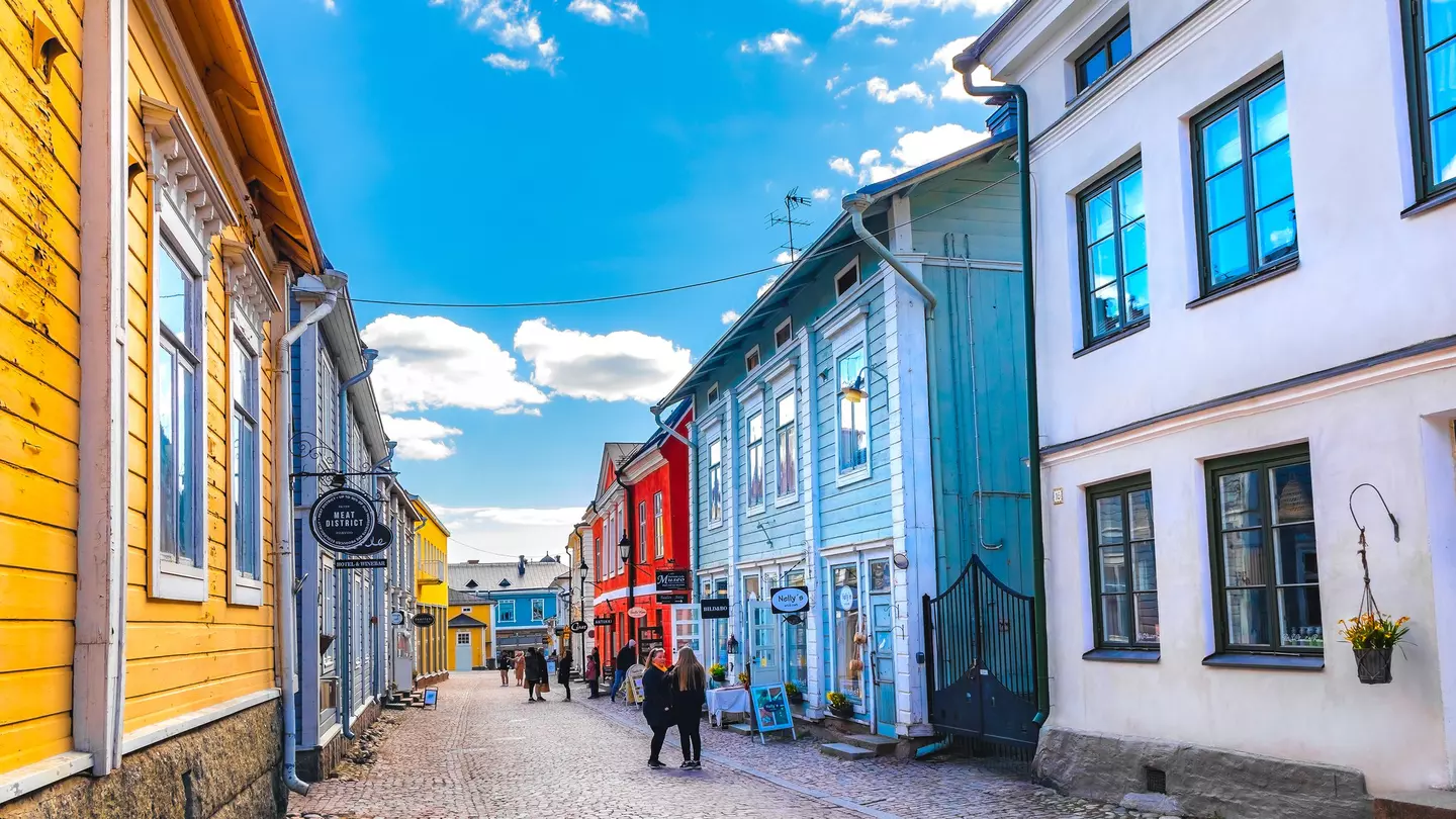 A street perspective with people walking by colorful wooden houses under a bright blue sky in Porvoo, Finland, Europe