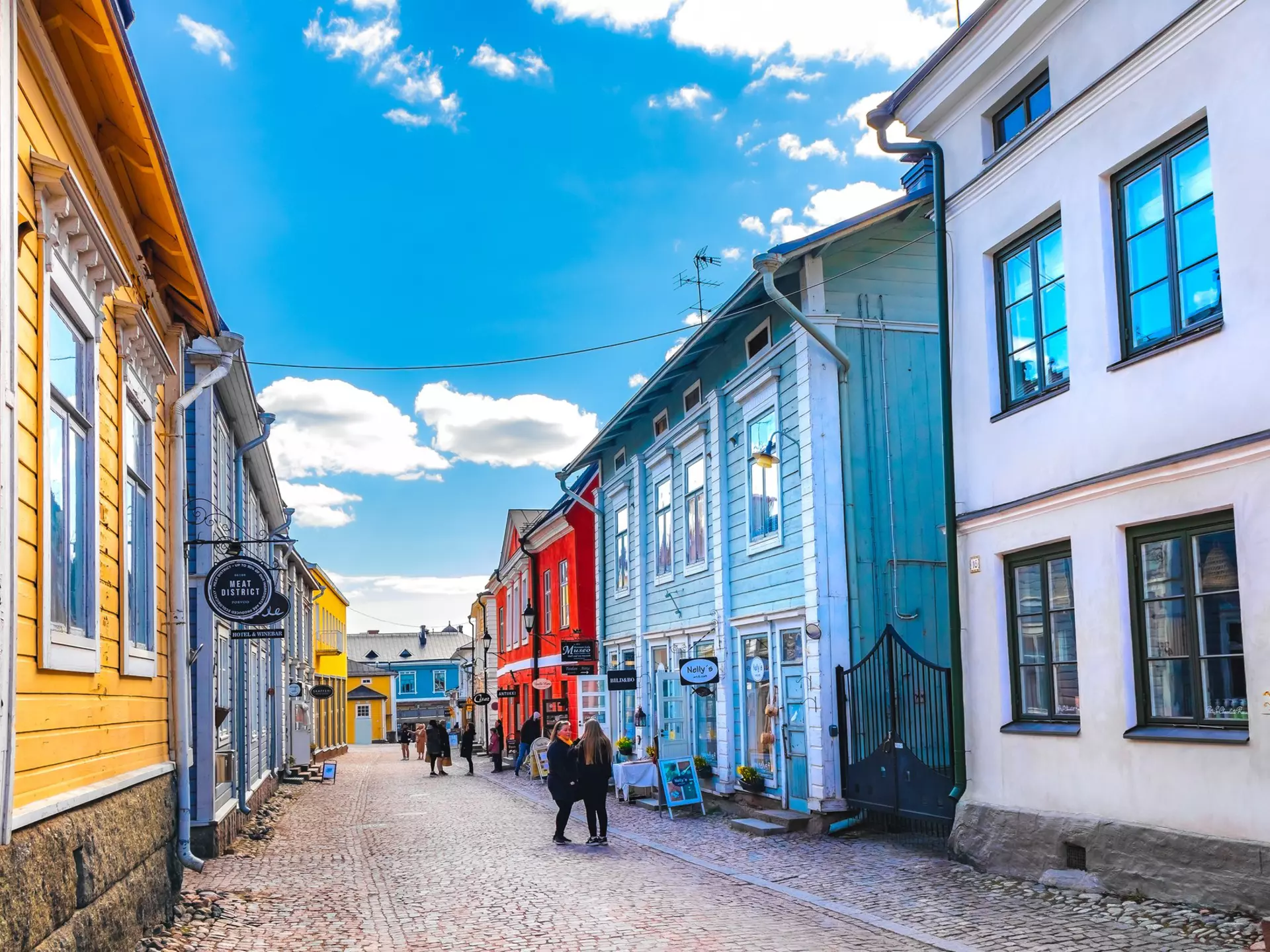 A street perspective with people walking by colorful wooden houses under a bright blue sky in Porvoo, Finland, Europe
