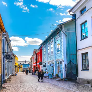 A street perspective with people walking by colorful wooden houses under a bright blue sky in Porvoo, Finland, Europe