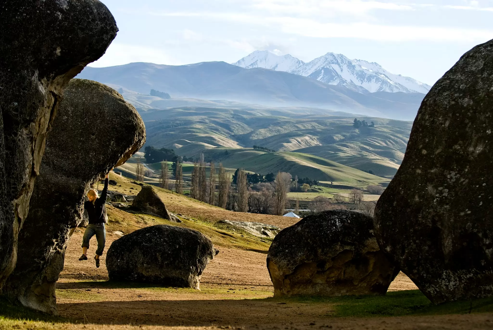 A man clings from limestone boulders with the mountains in the background.