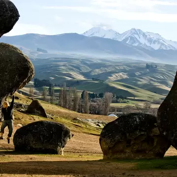 A man clings from limestone boulders with the mountains in the background.