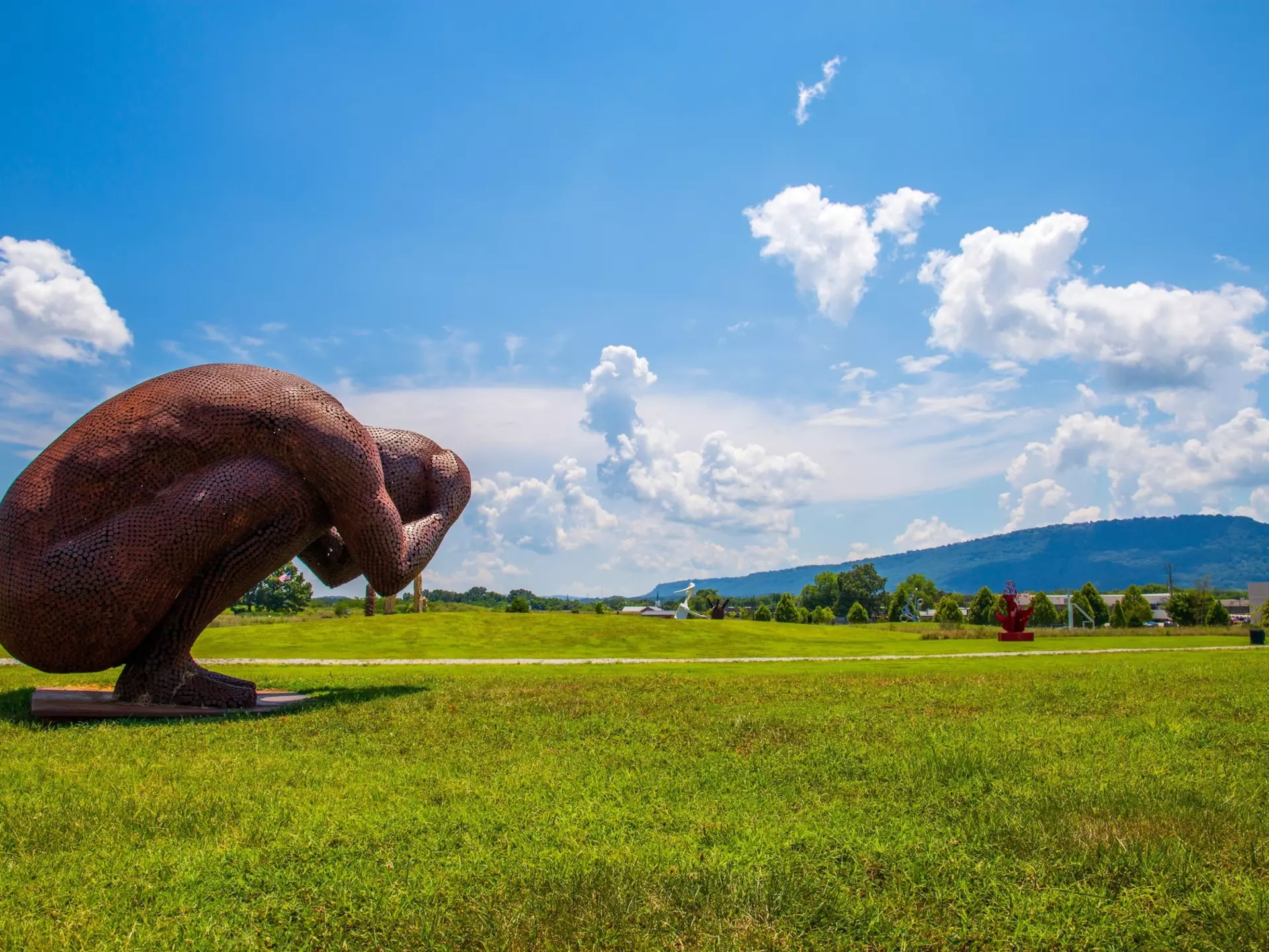 A large-scale outdoor sculpture made from coin-sized discs of corten steel in the shape of a man holding his head in his hands