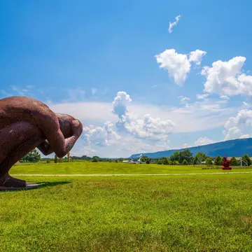 A large-scale outdoor sculpture made from coin-sized discs of corten steel in the shape of a man holding his head in his hands