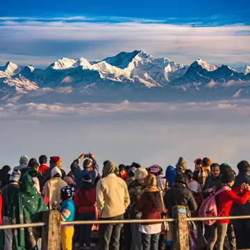 A large group of people gather at a viewpoint to watch the sunrise over a snow-capped mountain