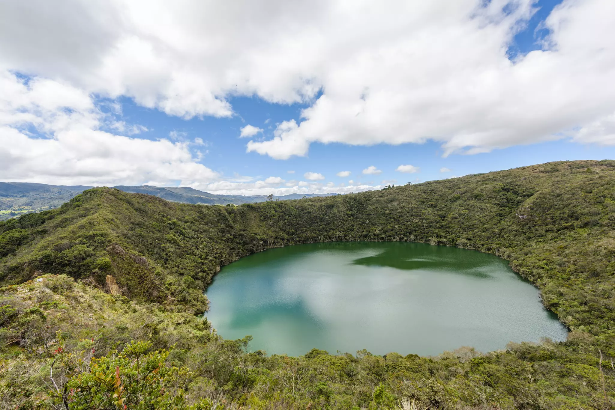 The brilliant green waters of Lake Guatavita contrast with the round cirque of mountainous terrain around the lake shot at a slight angle