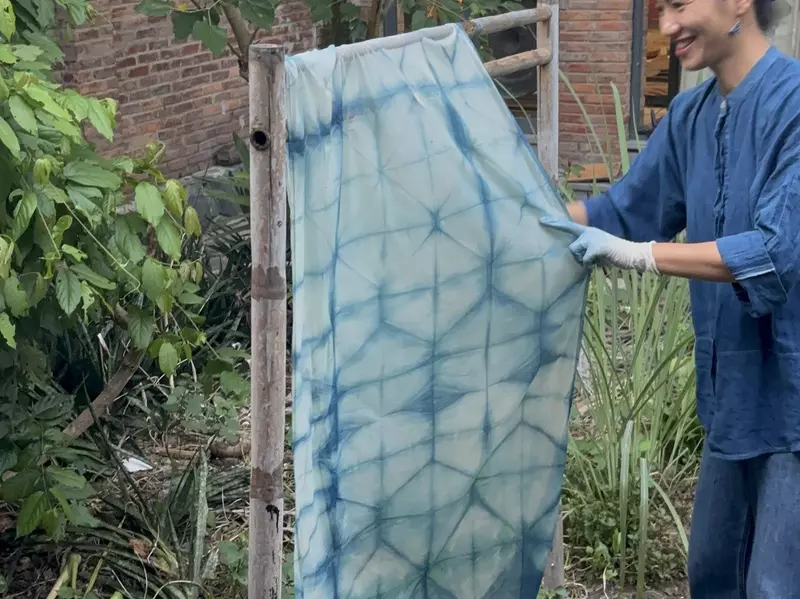 A woman handles a dyed piece of fabric on an outdoor rack