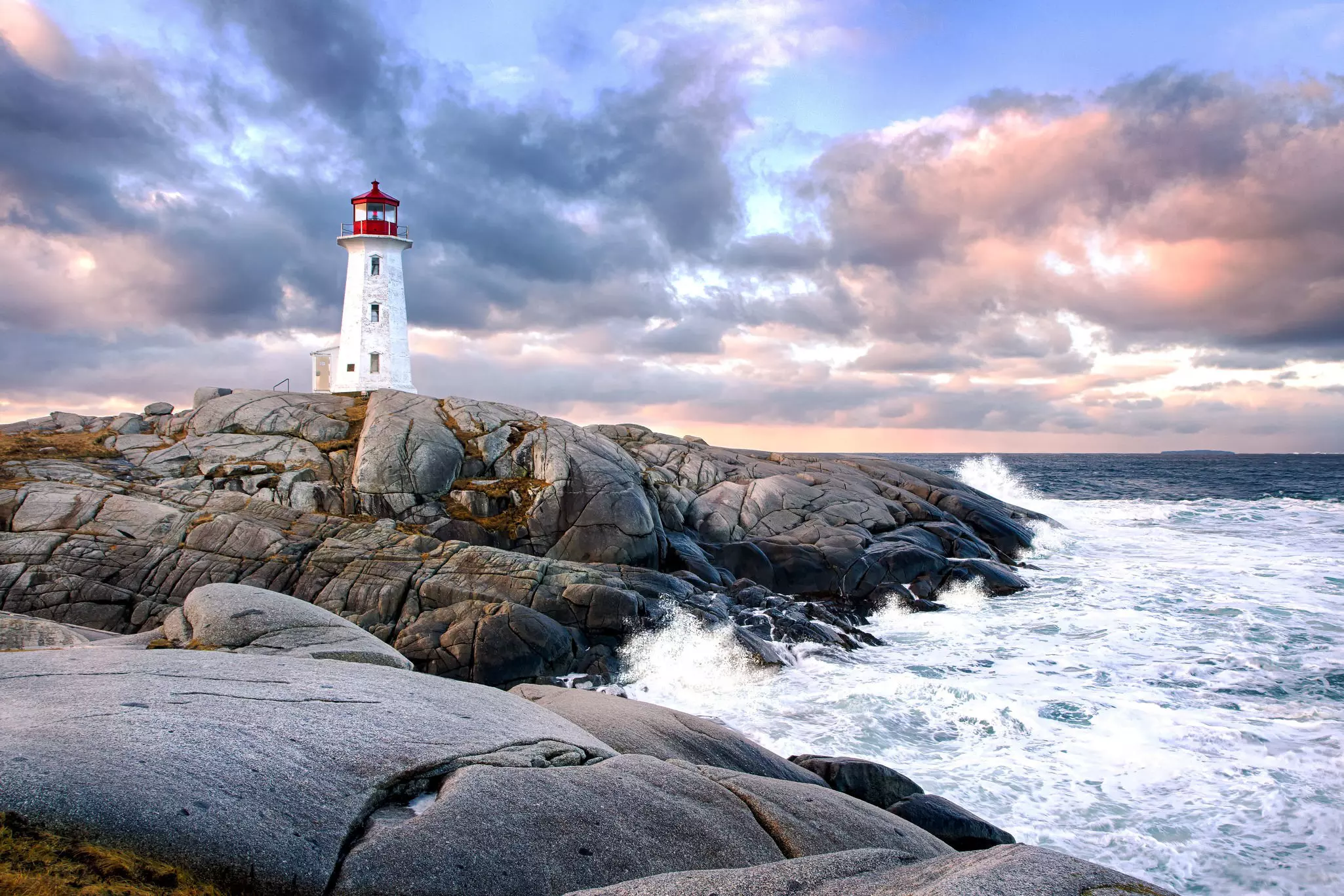 Peggy's Cove Lighthouse during sunset with waves crashing against the rocks.