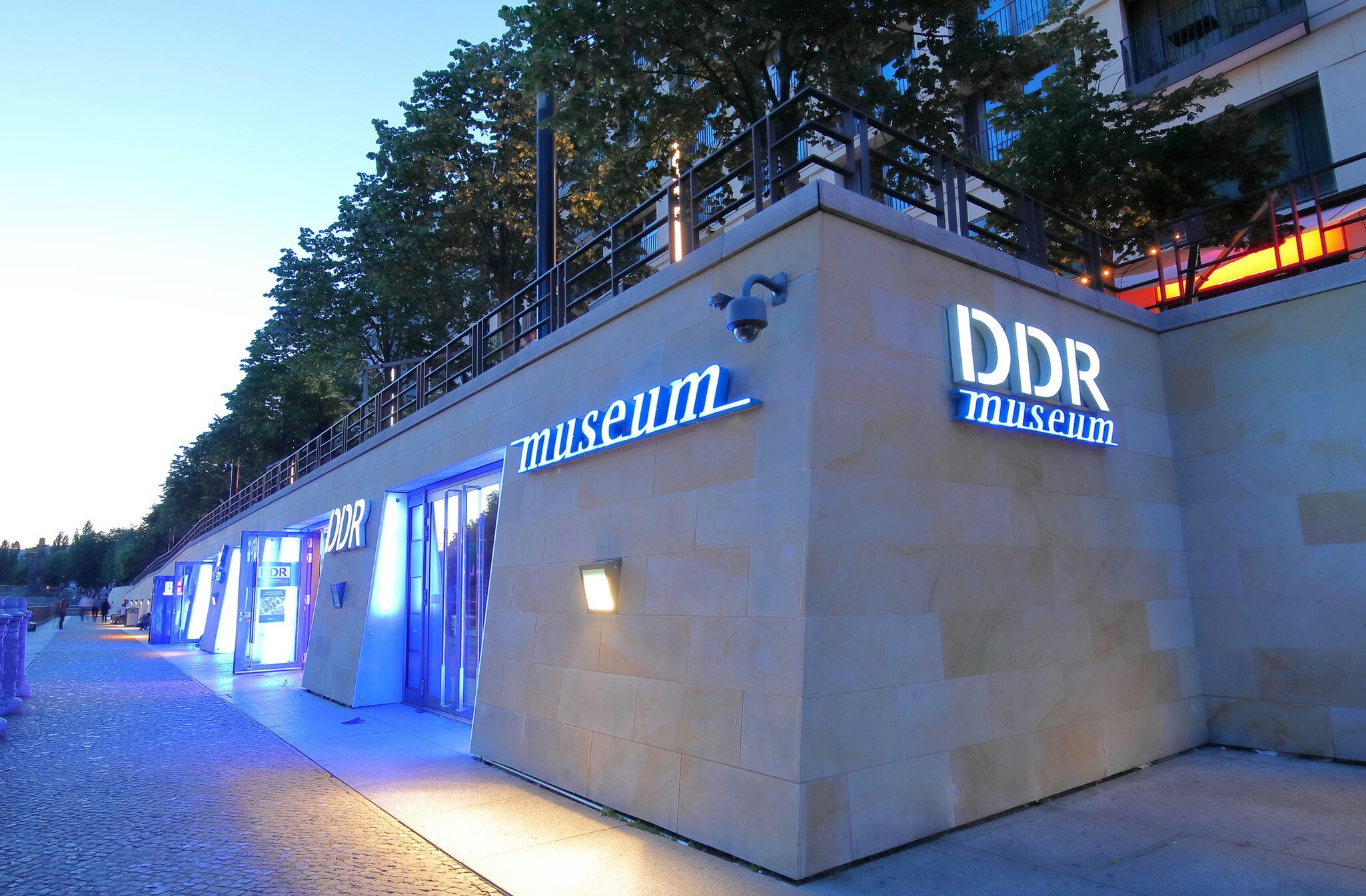 The exterior of the DDR Museum in Berlin, lit up with blue lights at night.