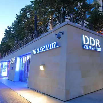 The exterior of the DDR Museum in Berlin, lit up with blue lights at night.
