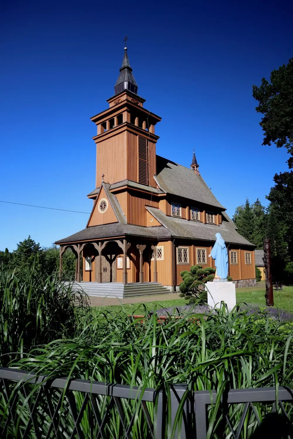 A historic wooden church stands in gardens with a blue statue nearby.