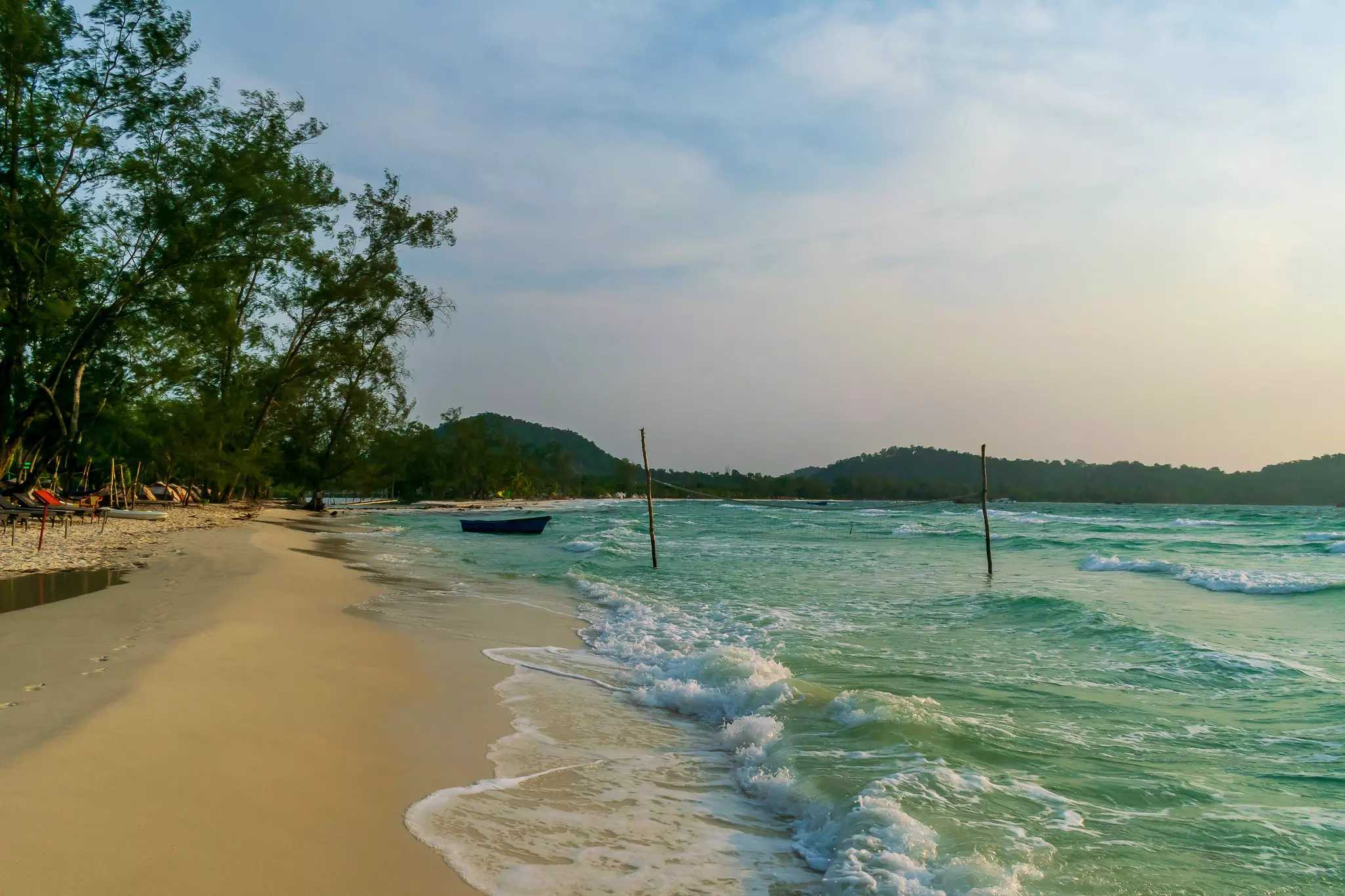 A boat floats in greenish water with low waves by a sandy beach.