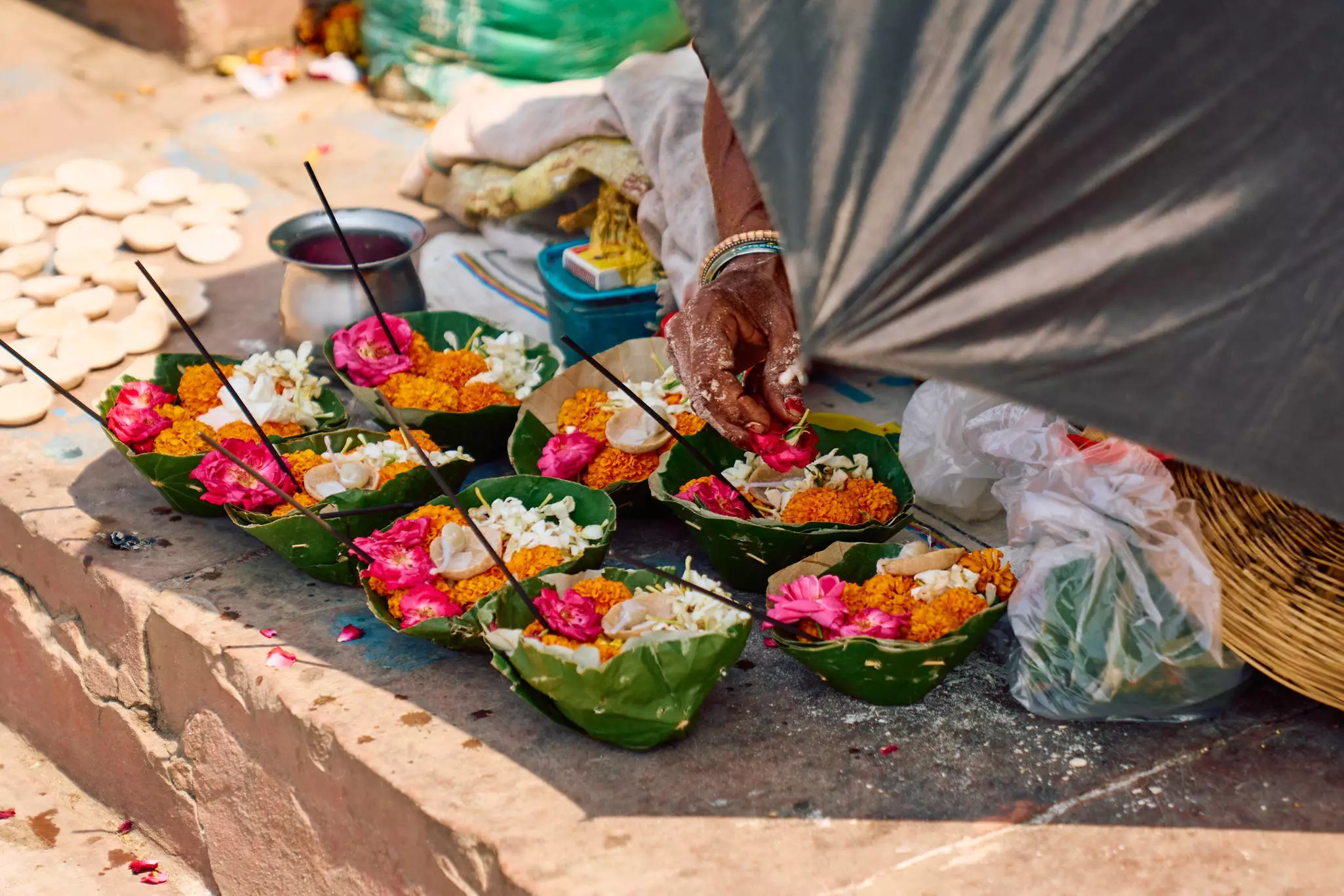 A vendor prepares a flower offering; there are two rows of similar offerings.