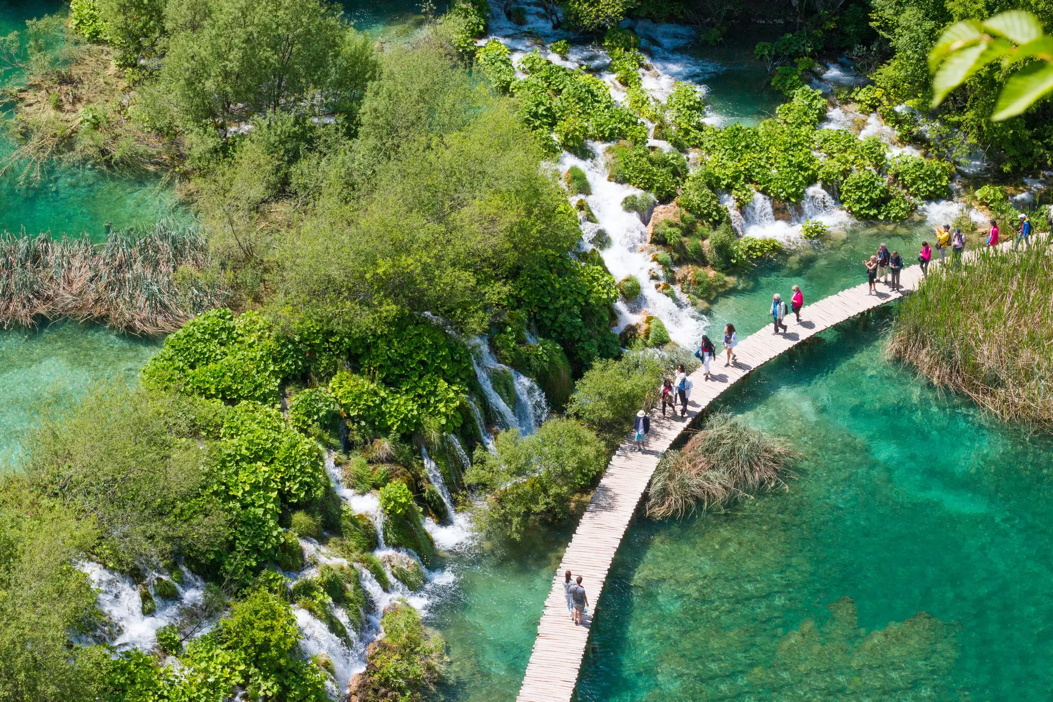 People walk over a lake via a wooden walkway