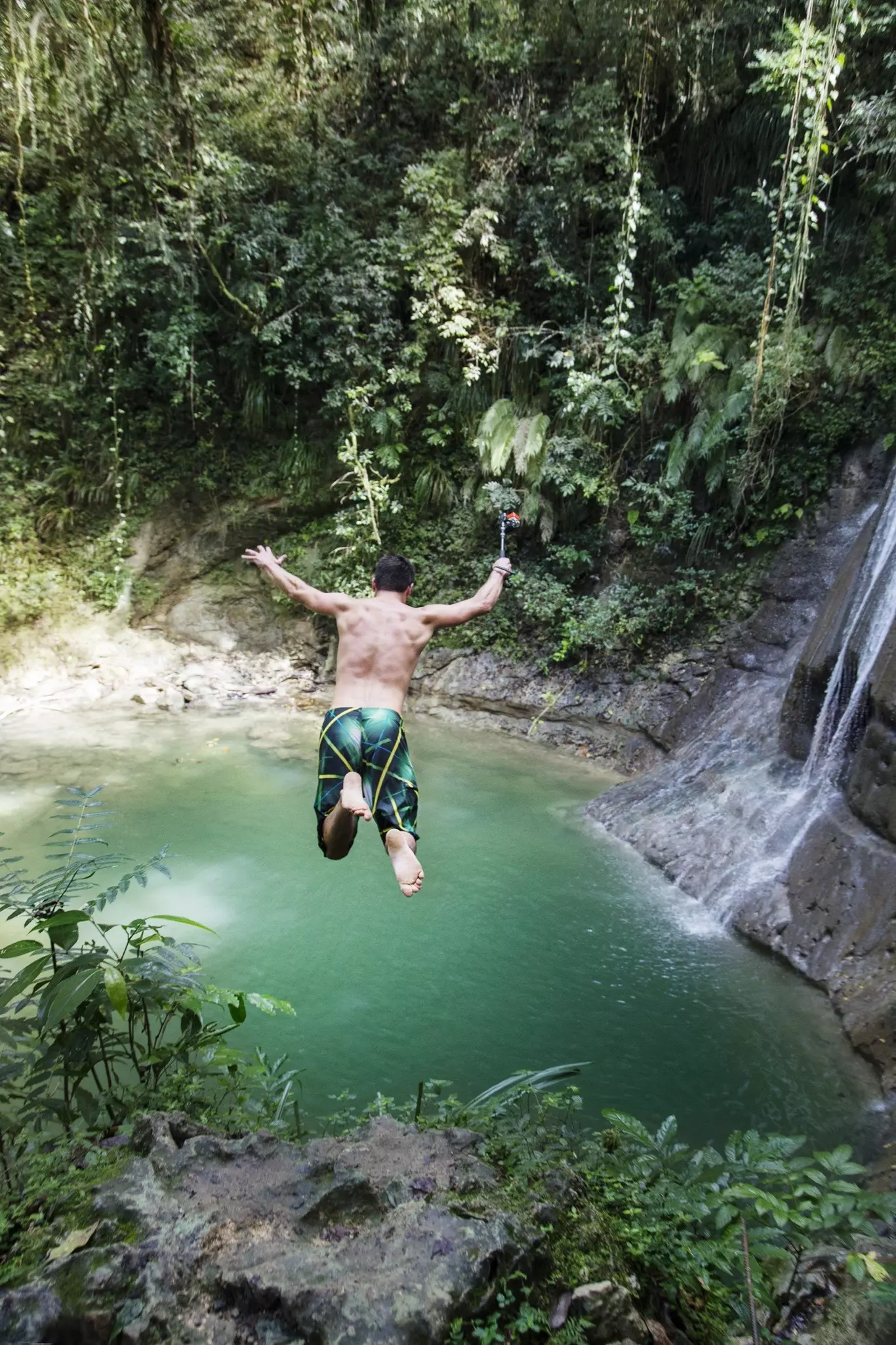 A man jumps off a cliff into a large pool below in a forest in Puerto Rico