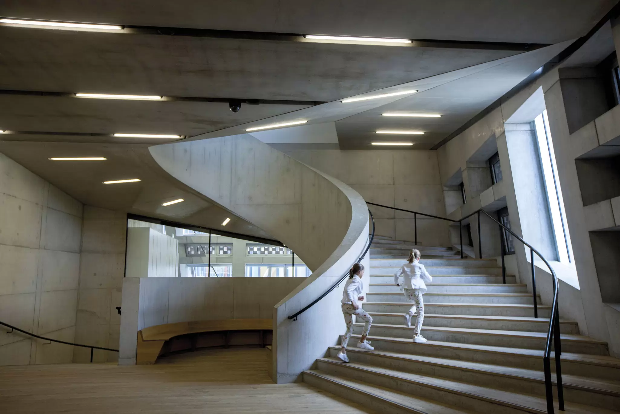 Two children run up a Brutalist-style concrete spiral staircase
