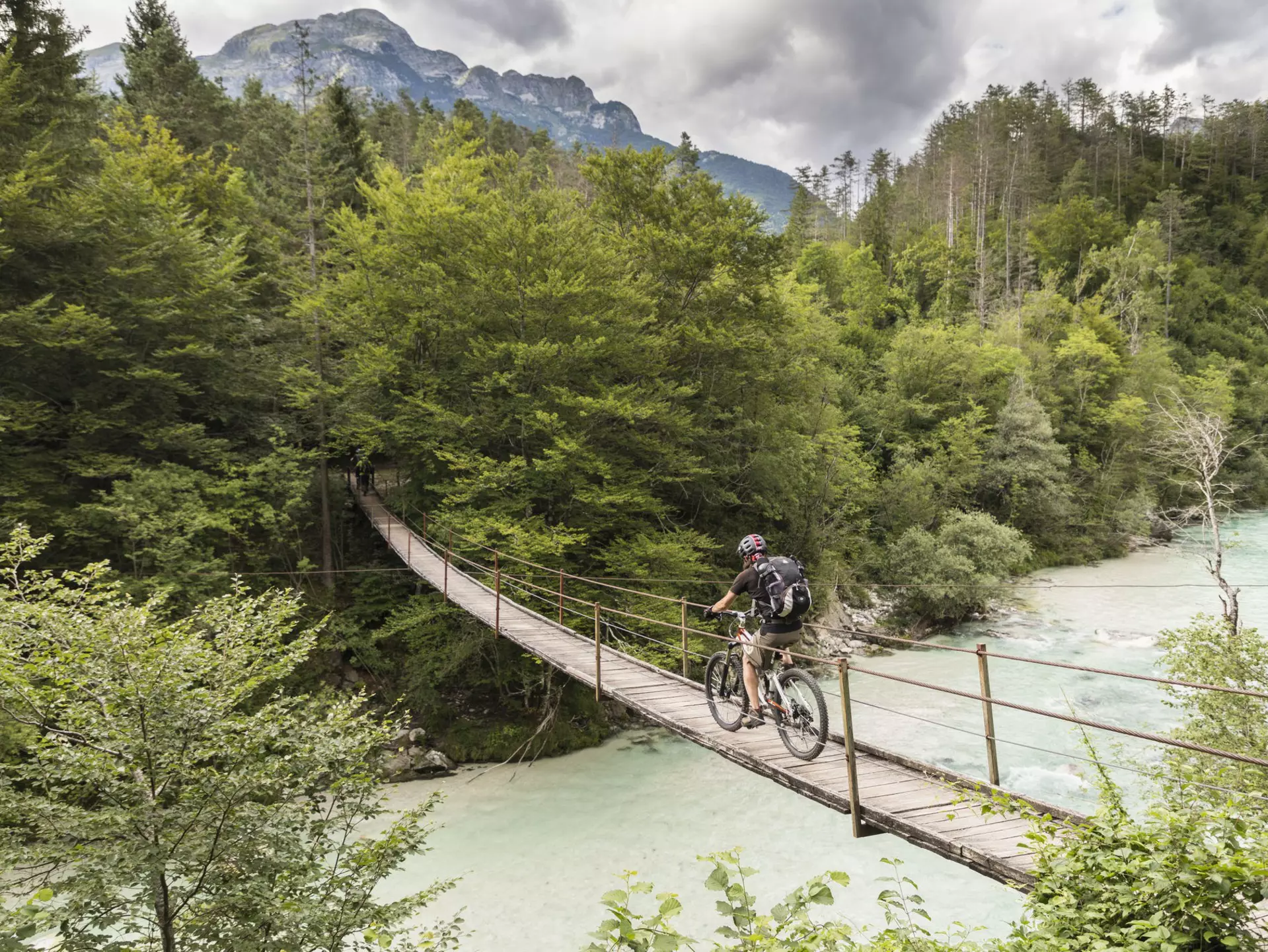 Mountain biker crossing a suspension bridge over the Soca River in the Julian Alps, Slovenia.