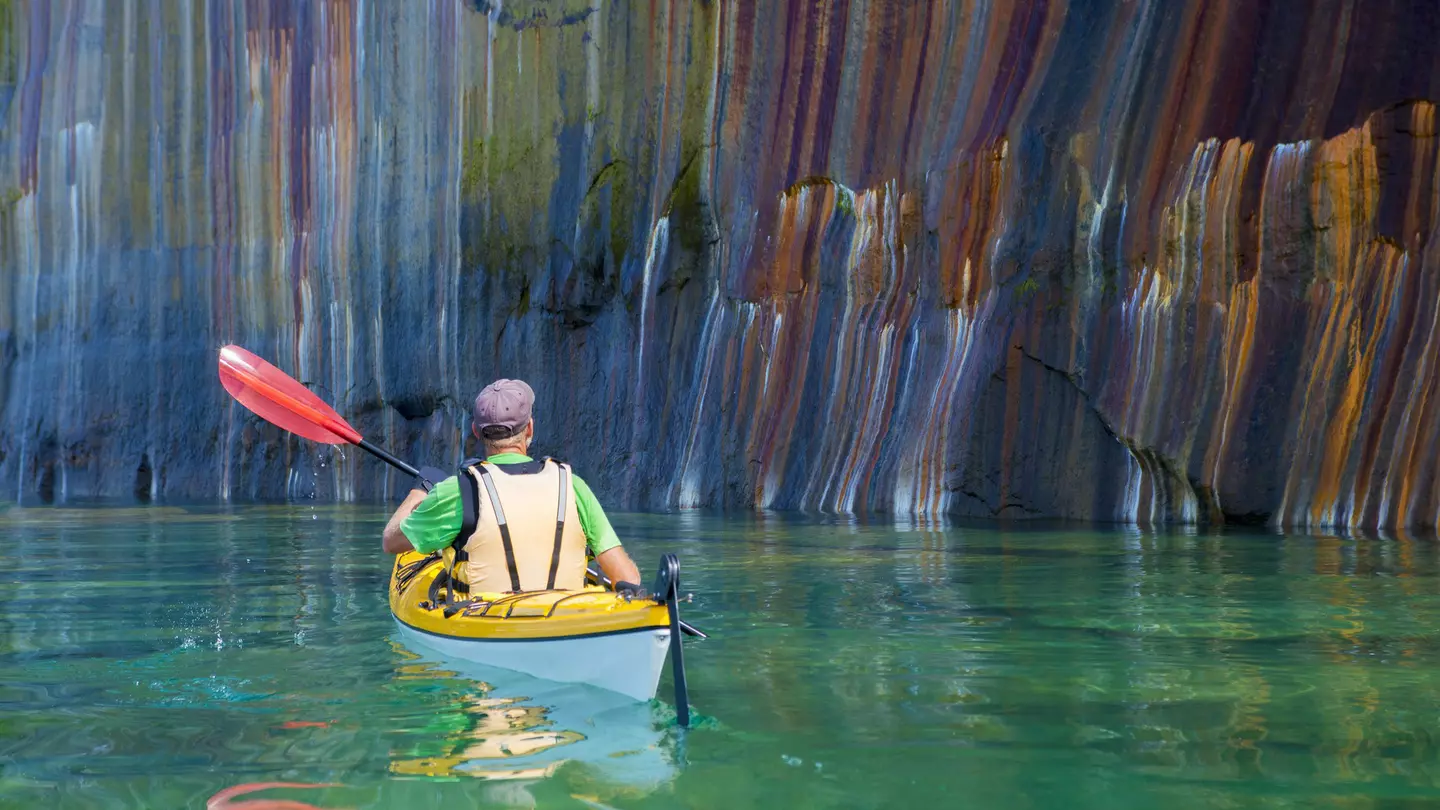 A man kayaking past a multi-colored cliff face in Pictured Rocks National Lakeshore, Michigan