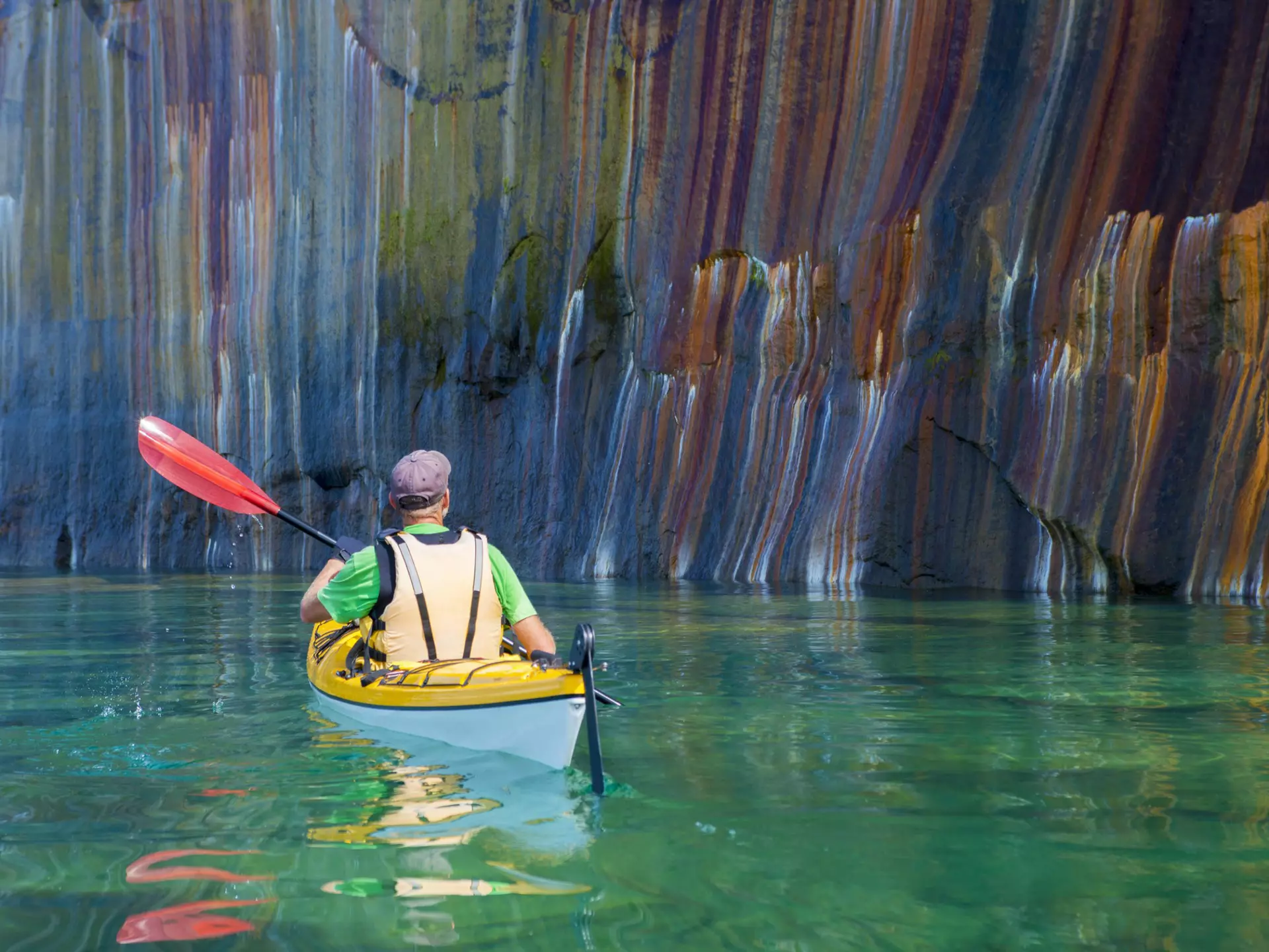 A man kayaking past a multi-colored cliff face in Pictured Rocks National Lakeshore, Michigan