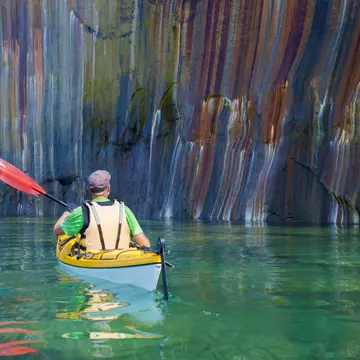 A man kayaking past a multi-colored cliff face in Pictured Rocks National Lakeshore, Michigan