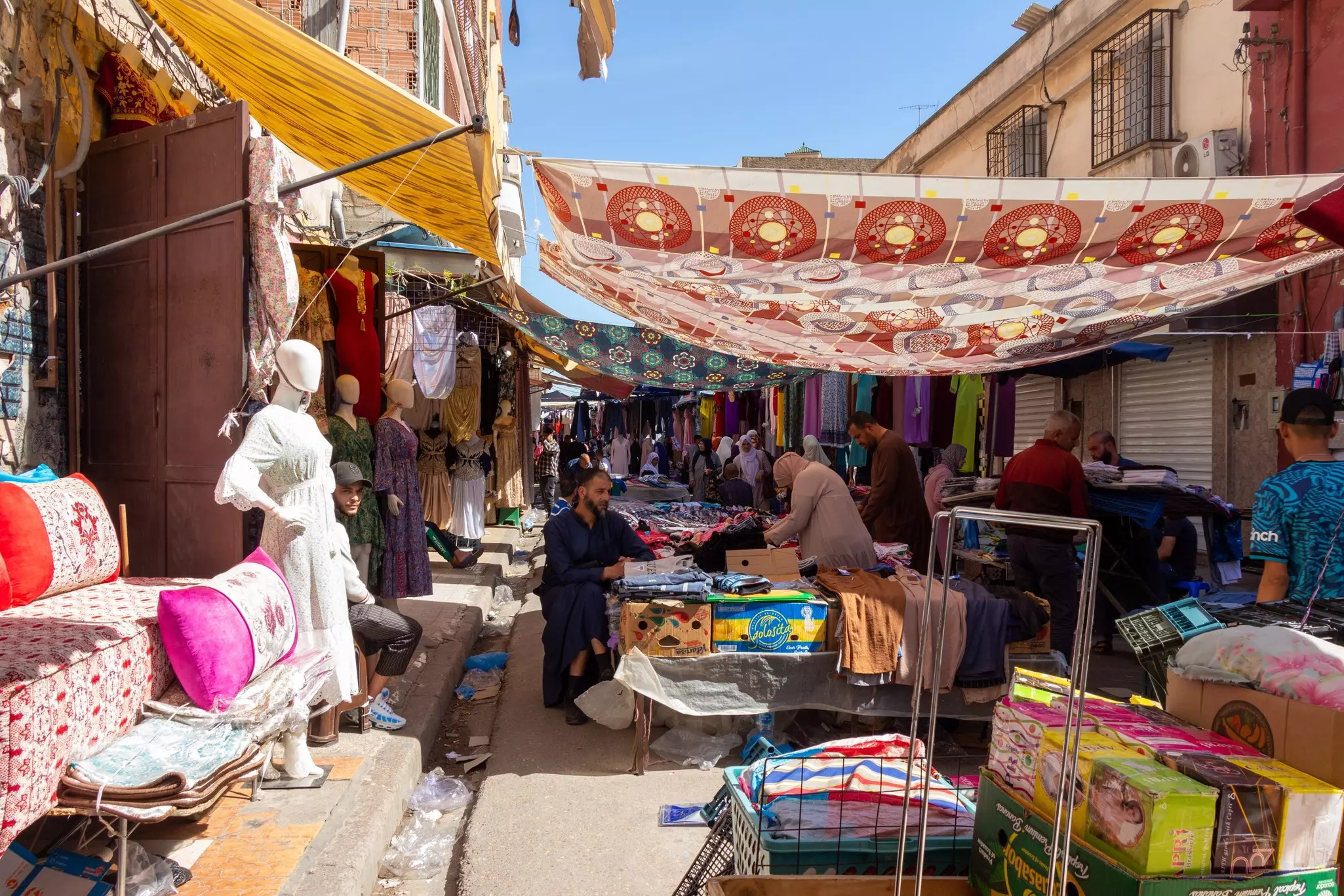 A busy market street with vendors selling clothes and fabrics.