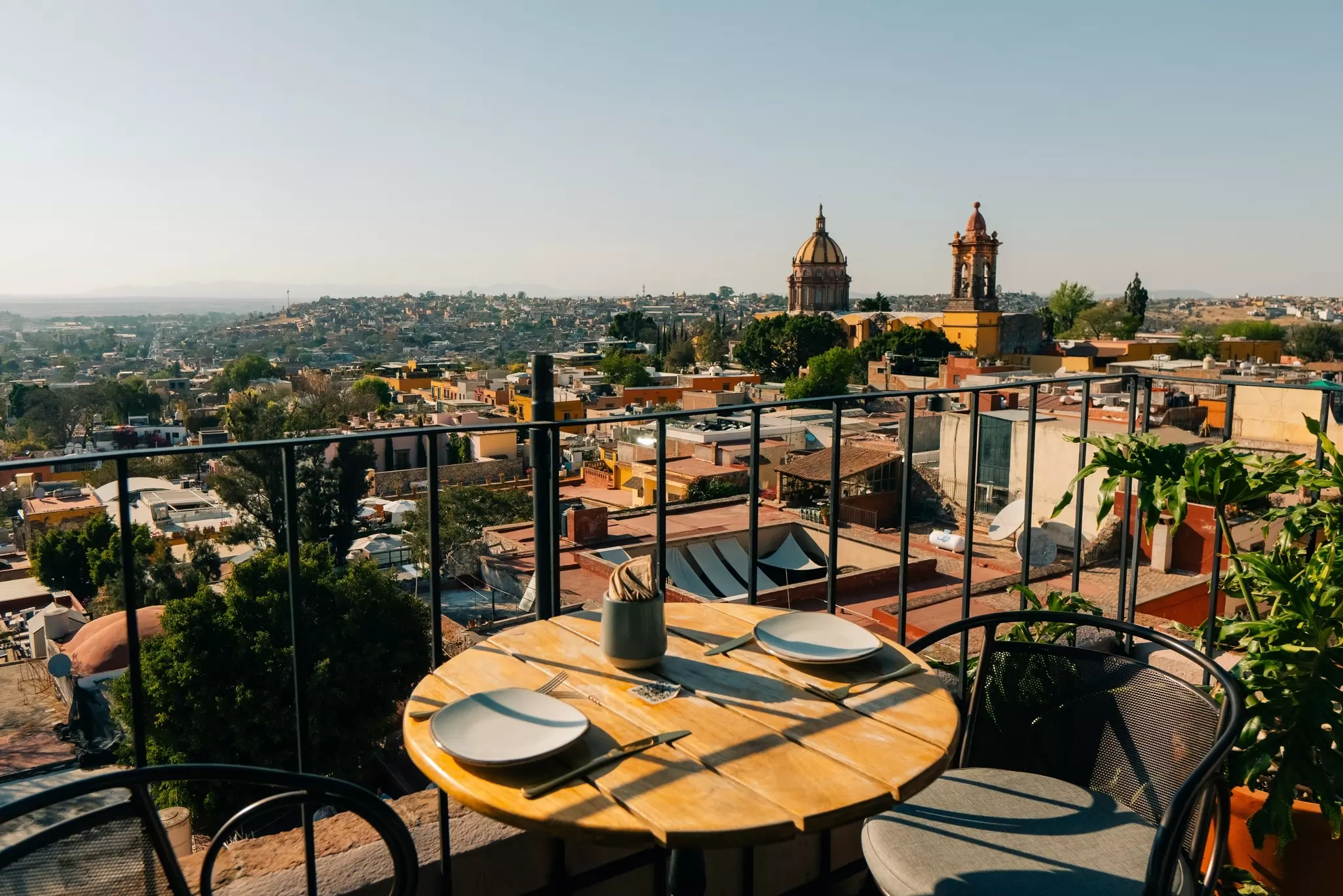 View of a city from a balcony that has a small table with plates on it and a chair next to the table