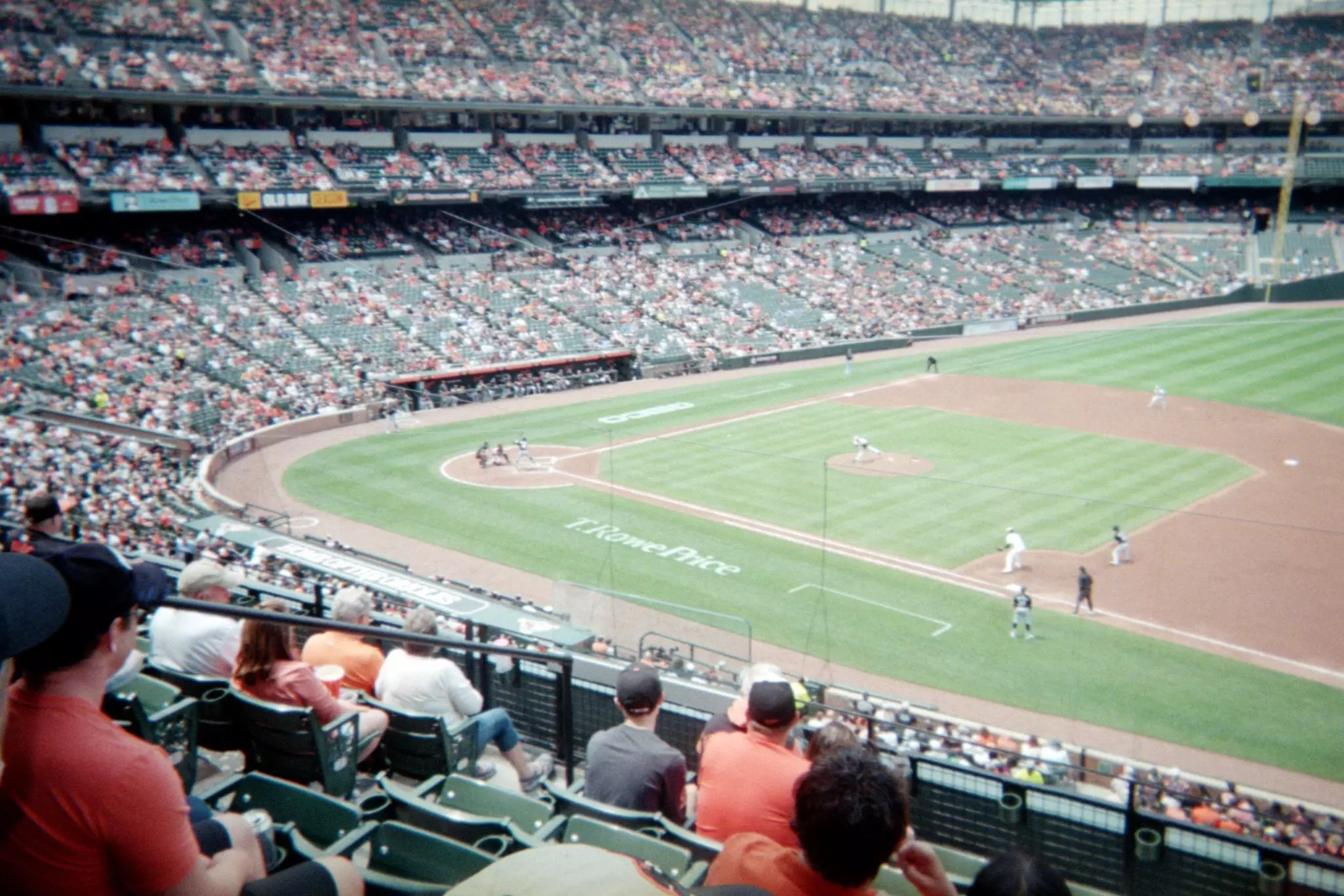 The view of a baseball stadium from the stands with players on the field and fans wearing orange