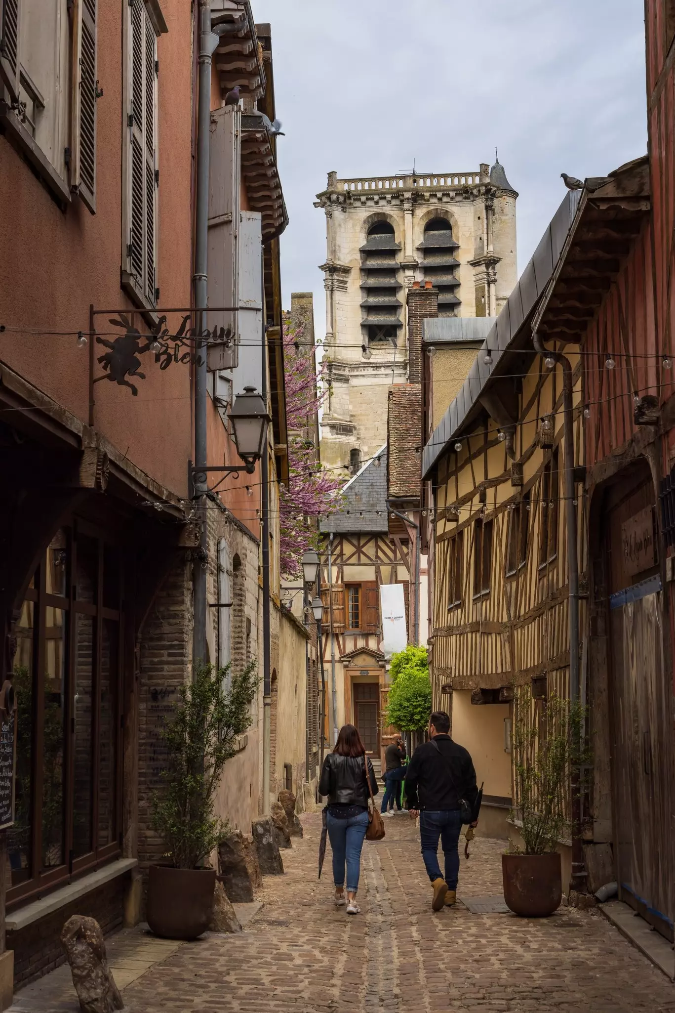 Two people walk down a narrow alleyway between leaning medieval buildings