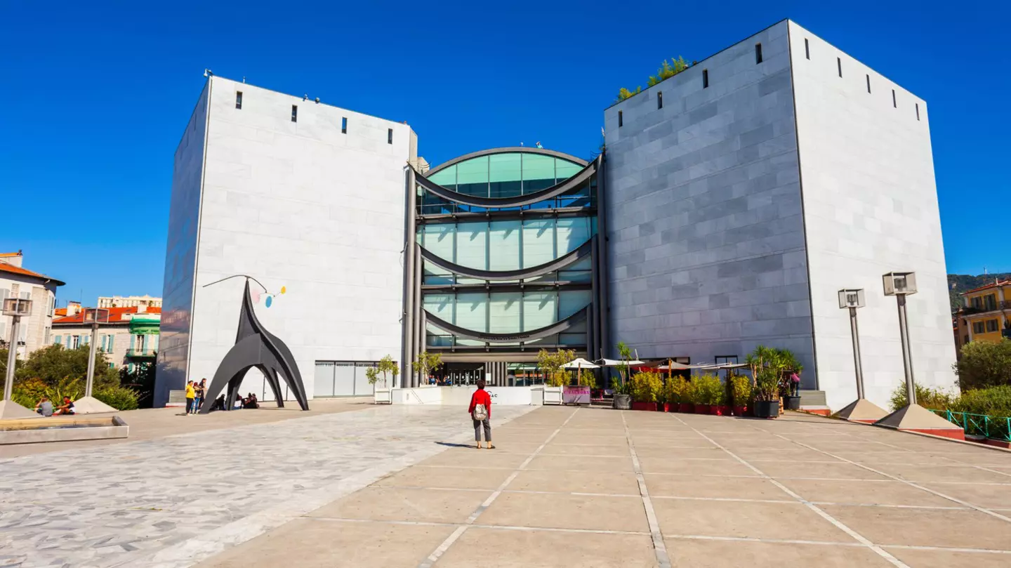 A solo figure stands looking towards a large modern building that houses Nice's Museum of Modern and Contemporary Art