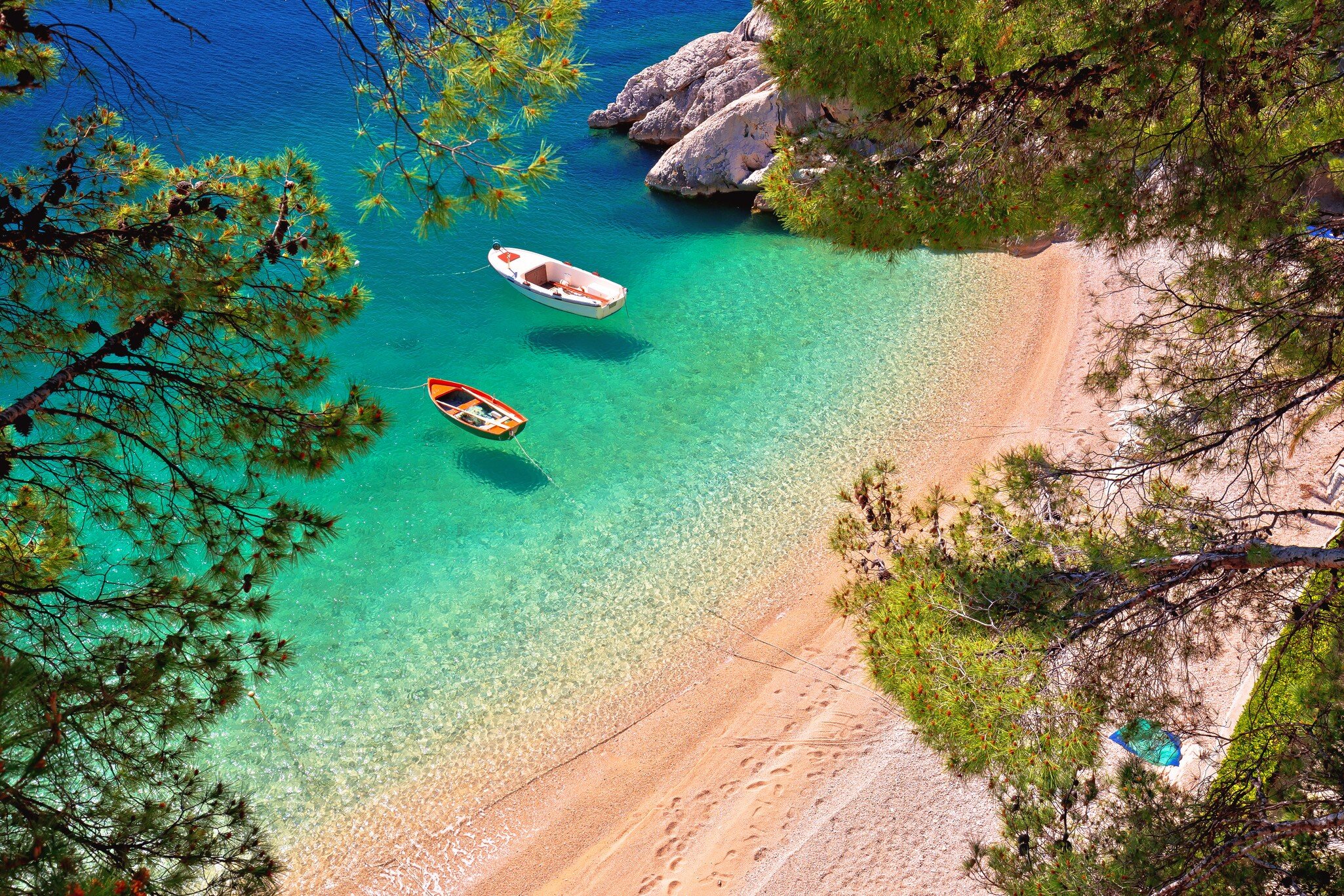 Aerial shot of cove with clear emerald-colored sea and two boats moored.