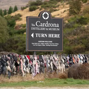 The Cardrona Distillery and Museum Sign Board with hundreds of Bras  hanging on the fence known as Bradrona, Bra Fence with hill background.; Shutterstock ID 1391917730; purchase_order: 65050; job: POIs; client: Lonely Planet; other: digital download