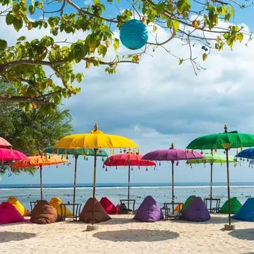 Colorful umbrellas and matching cushions on a sandy tropical beach.
