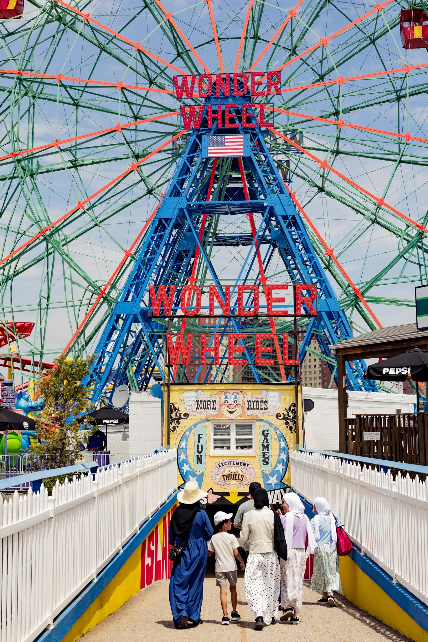 People walk toward a blue structure with a red sign reading "Wonder Wheel."