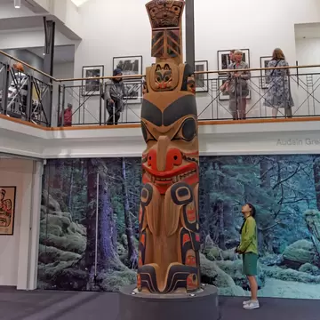 Young woman looking up at the James Hart totem pole in the Gallery of Northwest Coast Art, Vancouver, British Columbia, Canada.