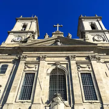 Granite church front with two clock and bell towers, saint statues and a cross above a large arched window in Porto