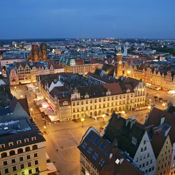 Gabled townhouses lit up around Wroclaw's Market Square at dusk, with the Old Town Hall tower and city rooftops beyond.