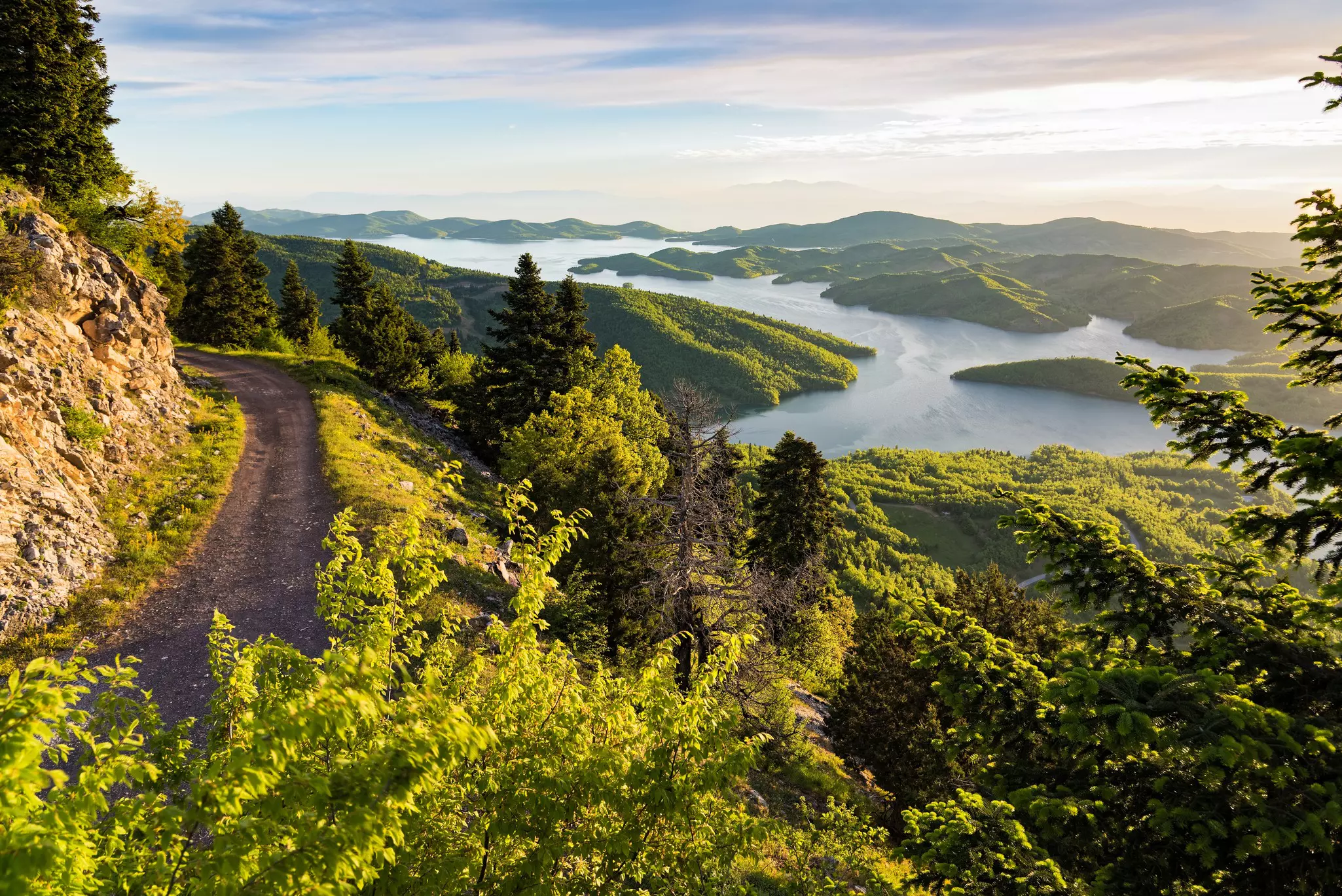 The sun rises over a lush green forest with islets in an artificial lake.