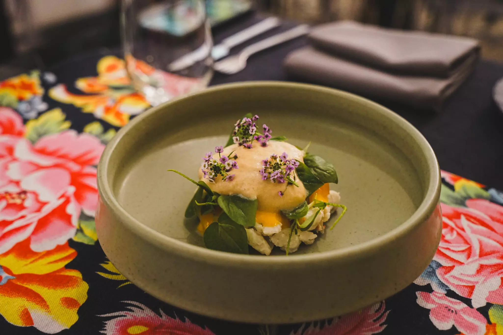 A green dish placed on a flower-patterned tablecloth contains a salad.