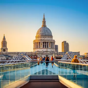 People walk over a bridge toward a large church at sunset.