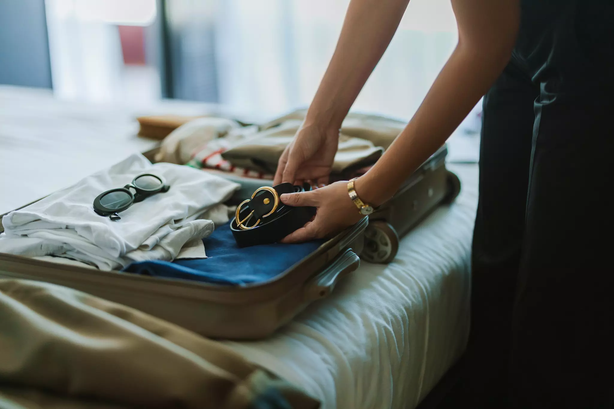 A woman placing a belt in a well-organized small suitcase that's open on a bed.