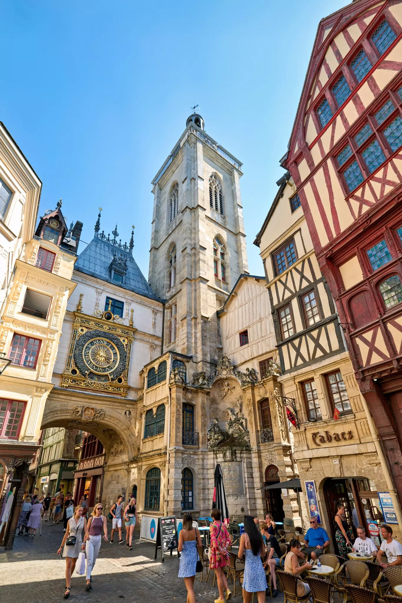 People walk through a medieval square framed by a giant clock